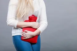 Vrouw met warme, rode kruik op de buik Vrouw met warme, rode kruik op de buik