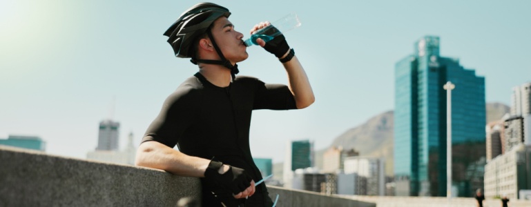 Man met fietshelm op drinkt uit een fles water
