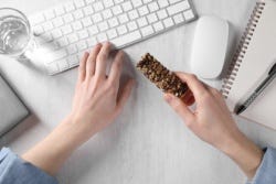 Iemand eet proteïnereep achter de computer Iemand eet proteïnereep achter de computer