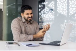 Man achter laptop houdt pijnlijke hand vast Man achter laptop houdt pijnlijke hand vast