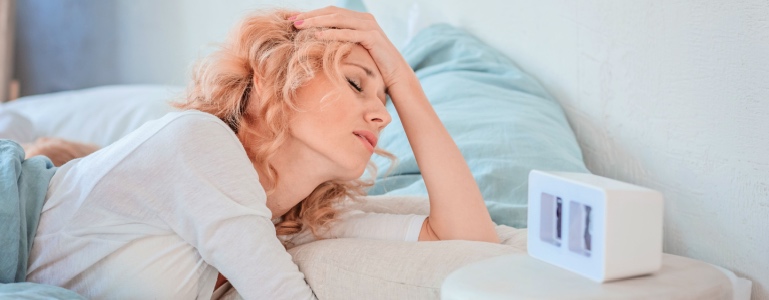 Vermoeide jonge vrouw kijkt wanhopig naar haar wekker